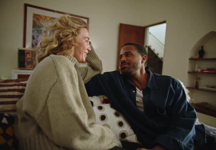 Man and woman laugh while sitting on couch together talking