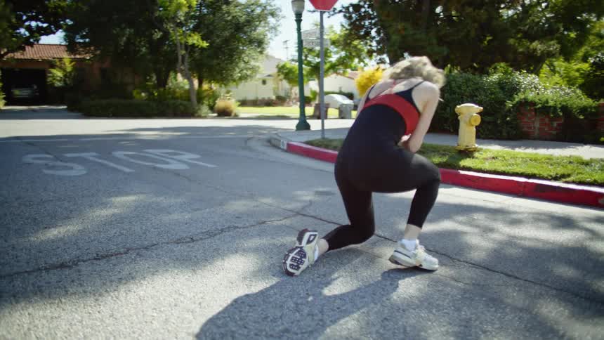 A blonde woman spins and stretches on a suburban road