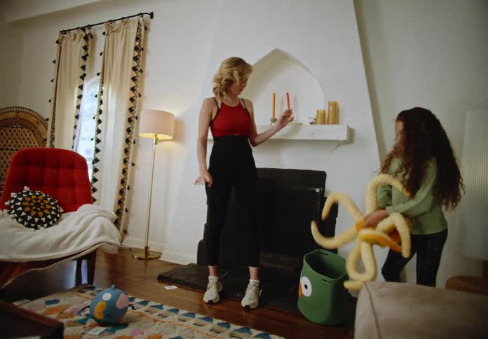 A child throws stuffed animals with her mother in a living room