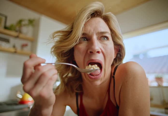 Portrait of a blonde woman eating cereal with a spoon and making funny faces