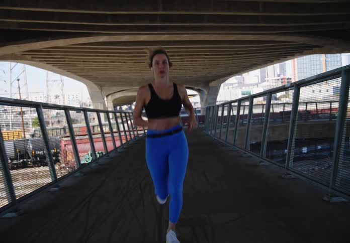 Fitness woman running on a bridge under a viaduct focused and determined