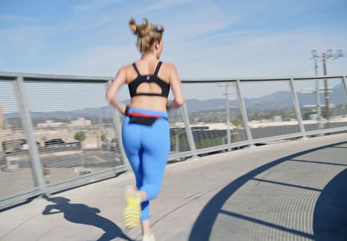 Woman wearing blue leggings runs along railing outdoors