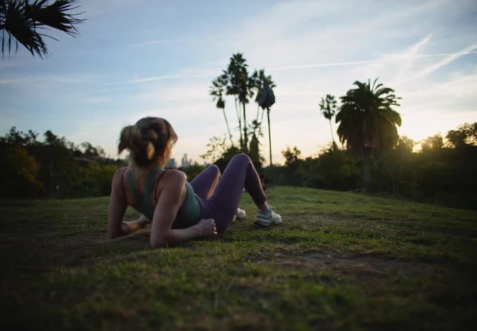 A woman sitting on the grass in the park admiring the sunset