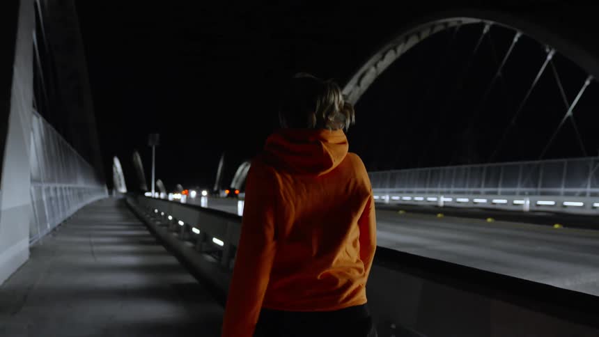 Woman walking on the side of a bridge at night