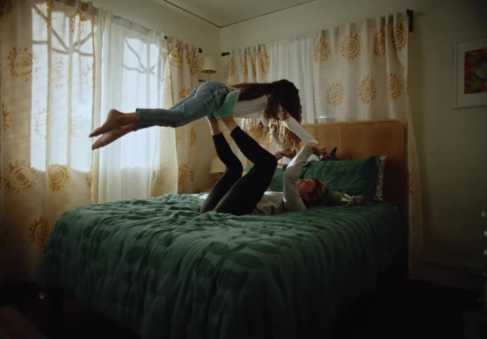 Mother and daughter playfully interacting on a bed in a room with light filtering through the curtains