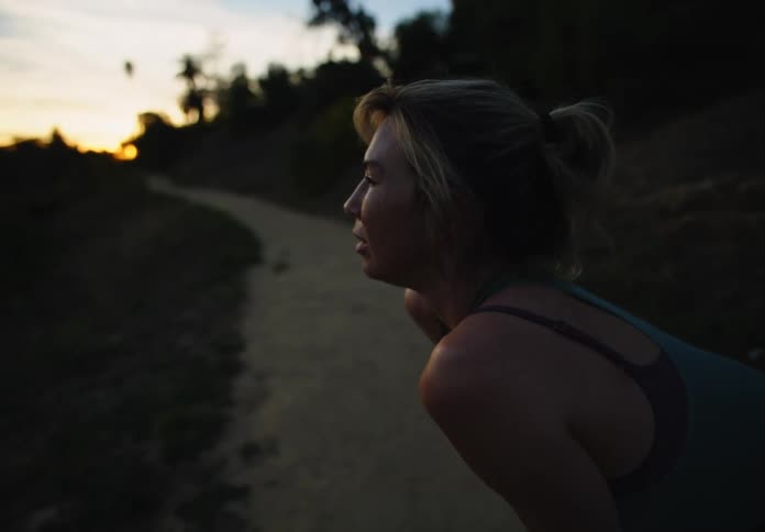 A woman resting after a sprint on a dirt path at sunset