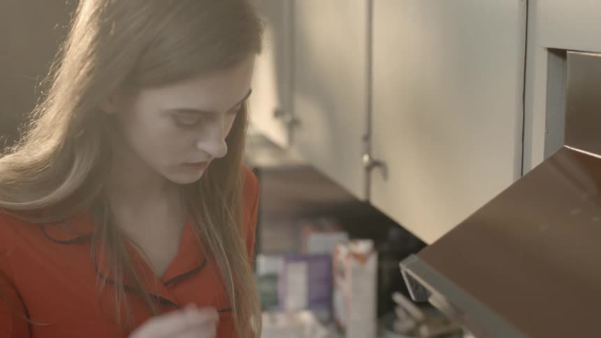A woman in a kitchen brushes back her hair