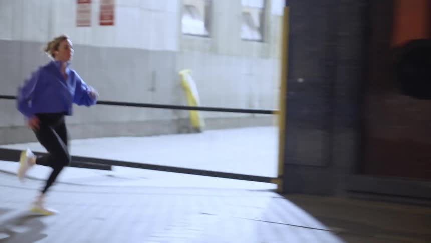 A fit woman wearing a blue jacket running on the sidewalk