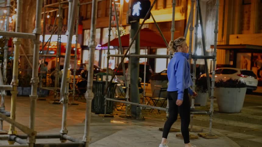 Woman running on a city sidewalk to the corner and then starting to stretch her legs