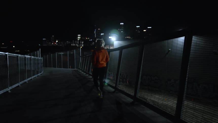 A person has his back turned and walks along a path with guardrails on his sides and then starts running
