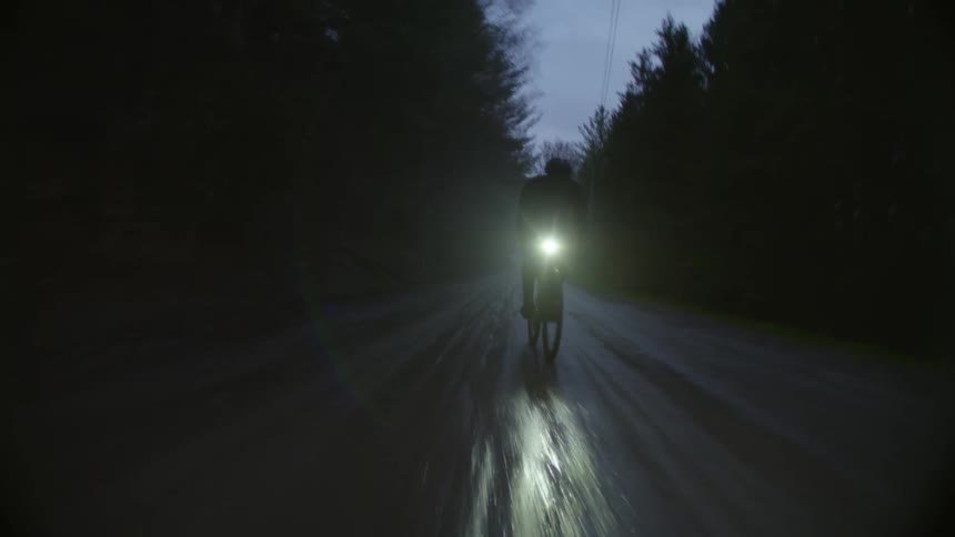 A person rides a bicycle down a wet road at night