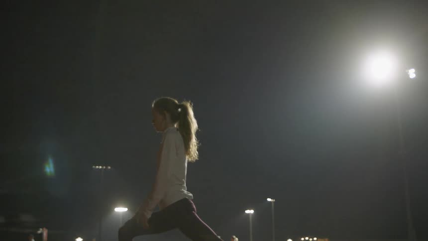 Woman stretches in a stadium at night