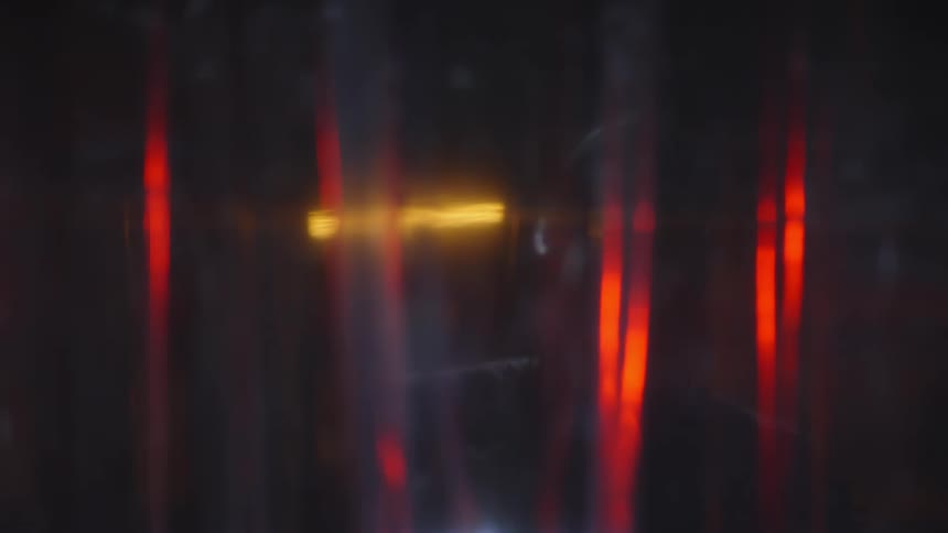 Person in a mask opening a transparent curtain and shining a flashlight in a dark room