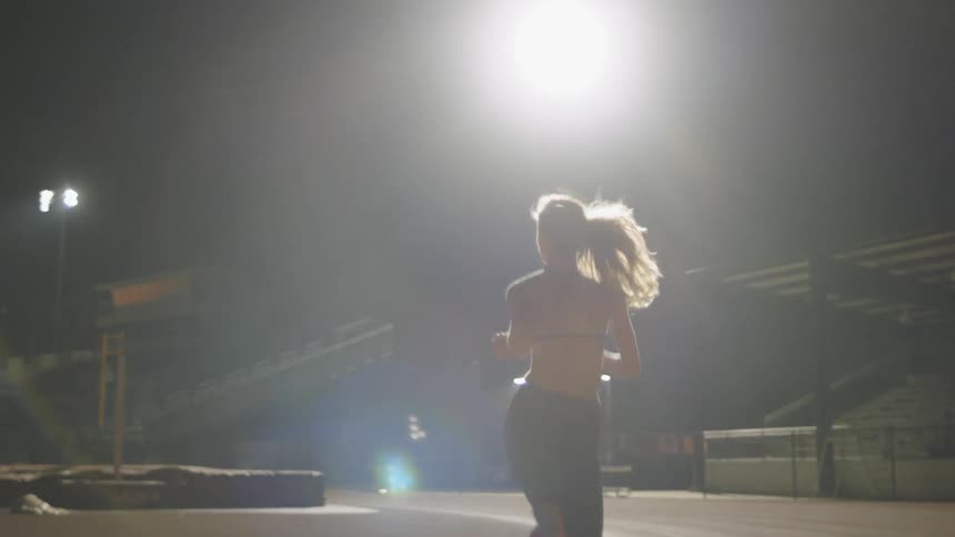A female athlete is running in a stadium at night