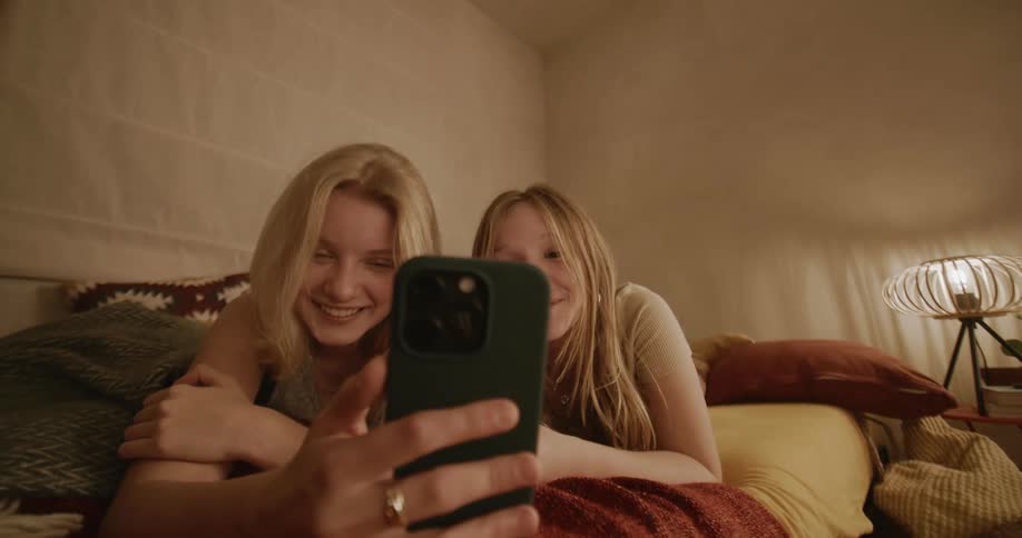 Woman and a young girl lying in bed smiling while they both look at their cell phones