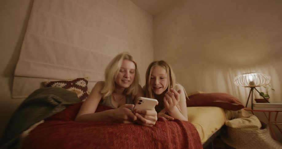 Two girls laugh while looking at their cell phone