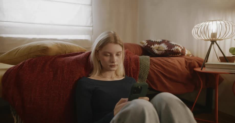 A teenager is using her cell phone in her bedroom