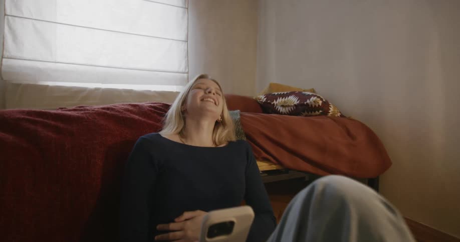 Happy teenage woman laugh looking at her phone in the bedroom