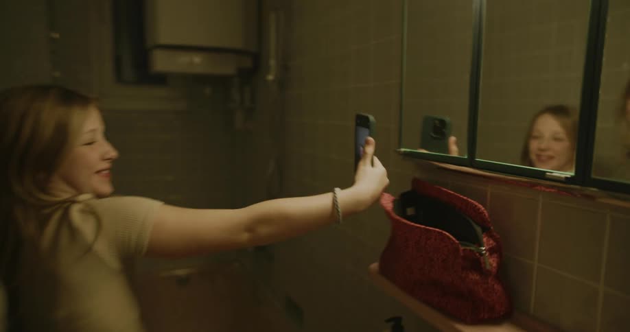 Two girls in a bathroom take selfies with a phone