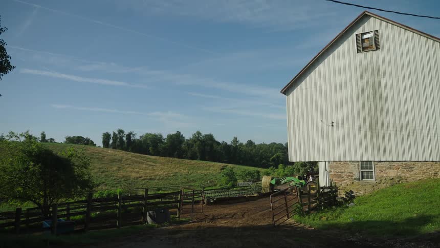 A rural scene with a large white barn in front of green fields and hills