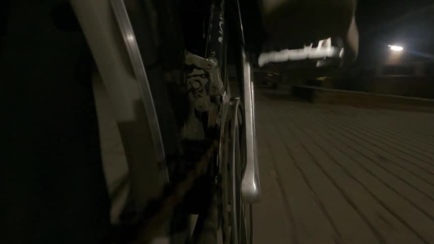 View of a chrome wheel of a bicycle and a person pedaling at high speed at night