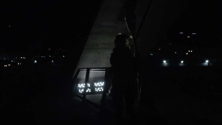 Female jogger runs on pedestrian bridge paralleling highway at night