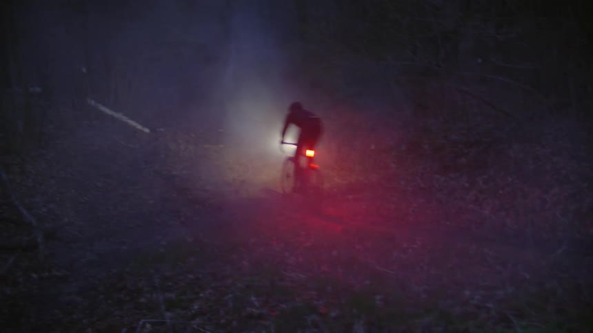 A person riding a bicycle on a trail through the forest at night