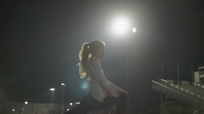 A woman is stretching outdoors at night