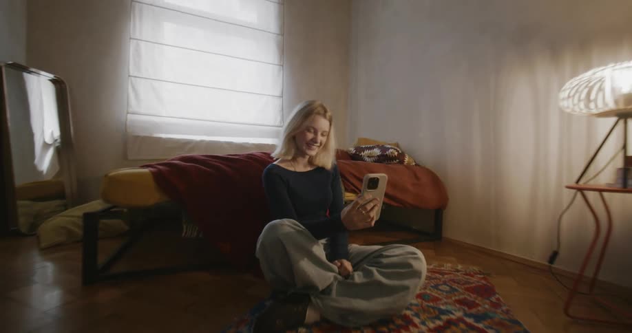 Young woman sitting on the carpet on the bedroom floor using her cell phone