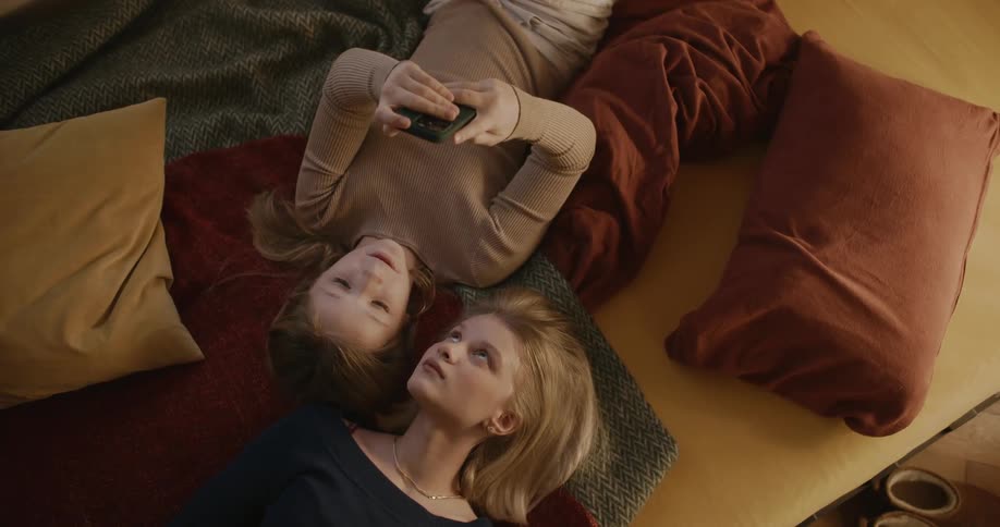A teenager and a child lying on the sofa talking and using their cell phones