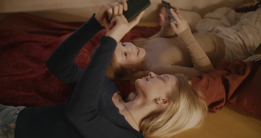 Two teenage girls fiddle with their phones and laugh
