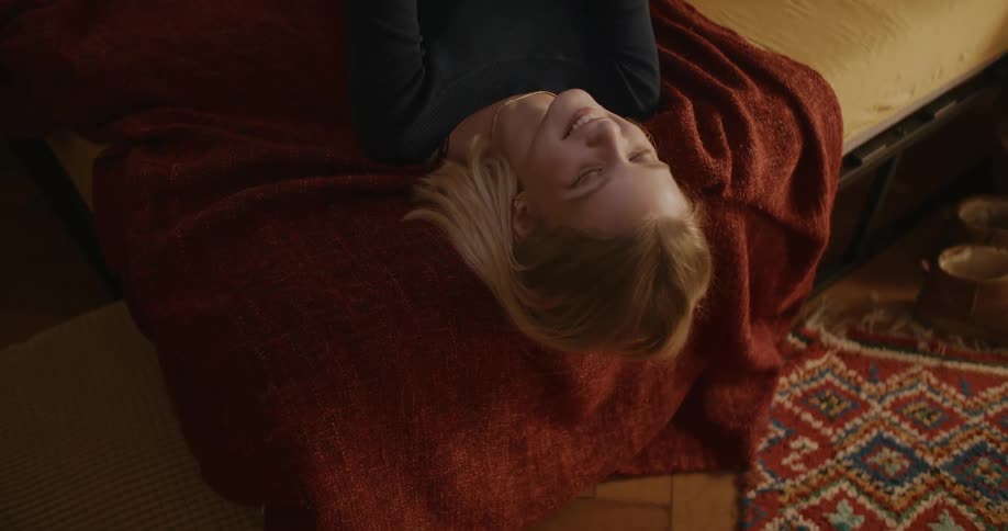 Young blonde woman lying in bed smiling while using her cell phone