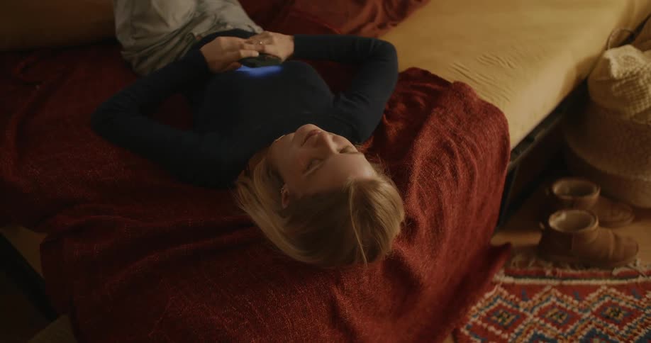 A teenager lies on a bed and uses a smart phone