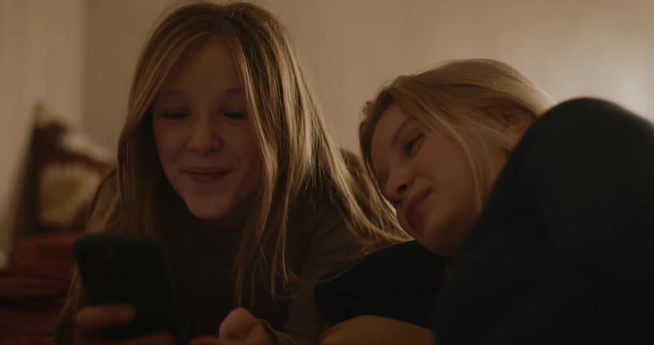 Portrait of a young woman and a teenage girl lying in bed playing on her cell phone smiling