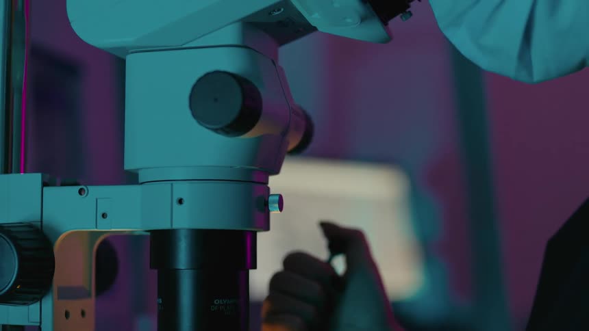 Concentrated woman looking into a microscope and at the same time applying a liquid with a needle into a small pot