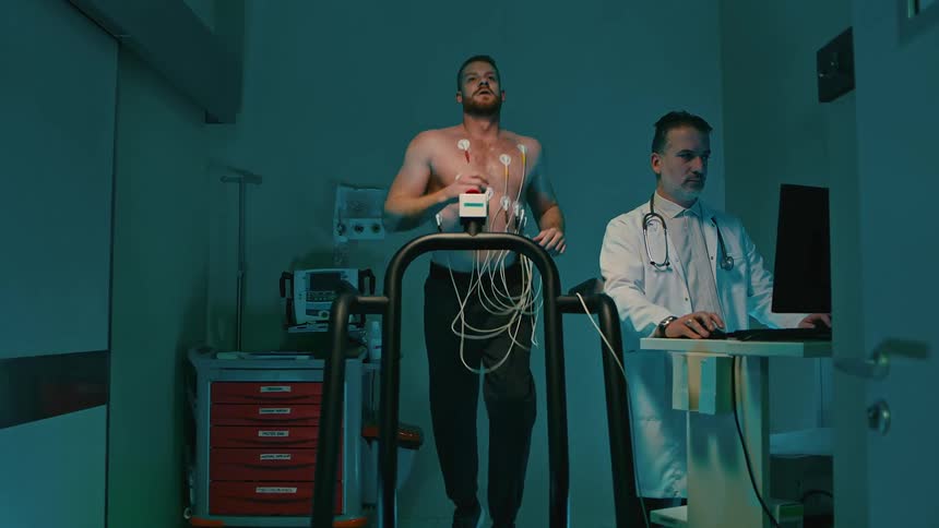 Doctor views computer monitor as male patient wearing sensors runs on a treadmill