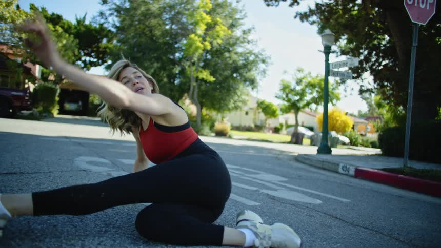Blonde woman in fitness clothes sitting on the street asphalt getting up stylishly