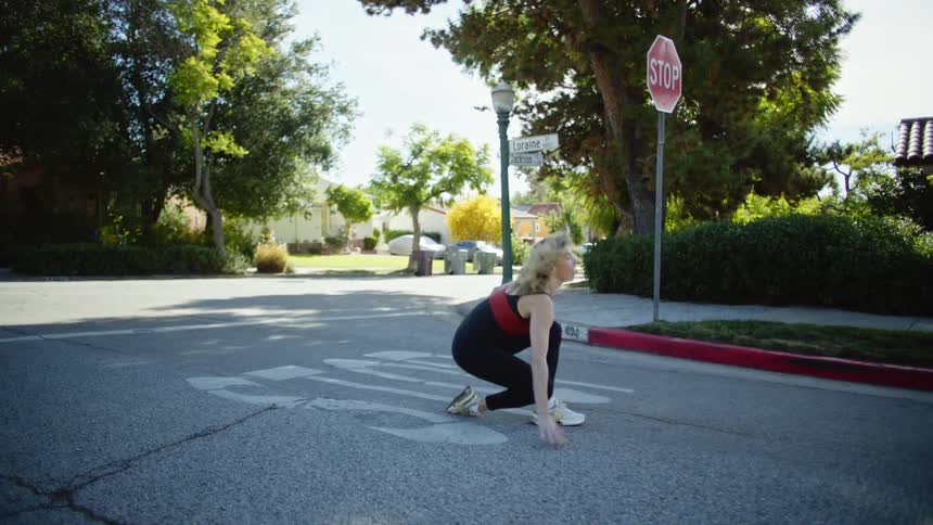 A woman in a leotard spins and dances in the middle of the road at an intersection