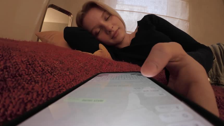 Young woman lying in bed taking out her cell phone and scrolling