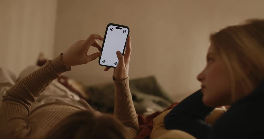 Portrait of a young woman and a child playing on their cell phones while lying in bed smiling