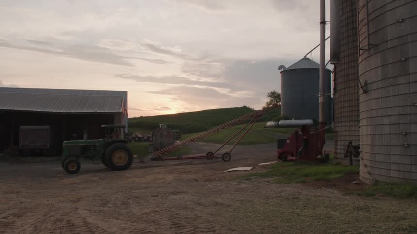 A farm worker drives the tractor near the silo