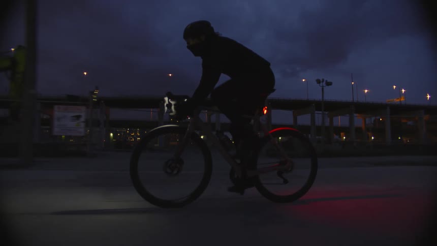 Silhouette of a person riding a bicycle near the city at night
