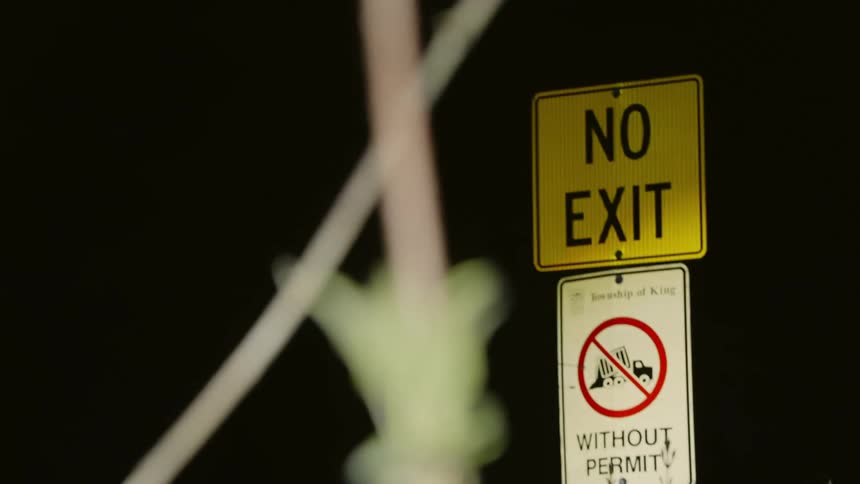 Two traffic signs on a pole illuminated by flashing lights at night