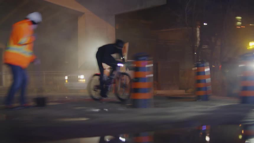 Man passing at high speed with a bicycle in the middle of an overpass undergoing renovations at night