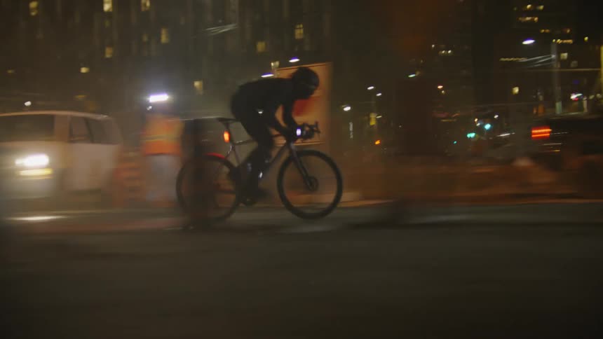 Man cycling at high speed through an alley in a metropolis at night