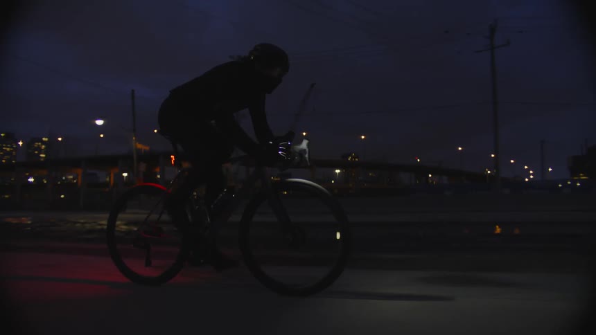A man driving a bicycle at night next to the city