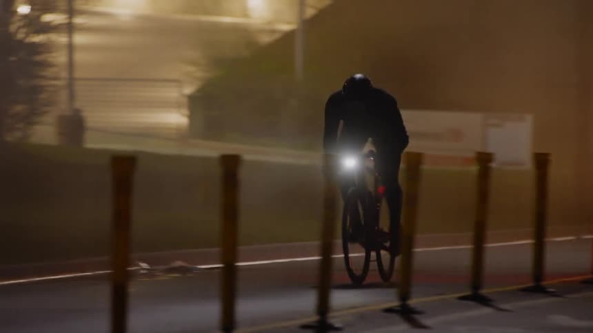 A cyclist on a street at night chasing a car