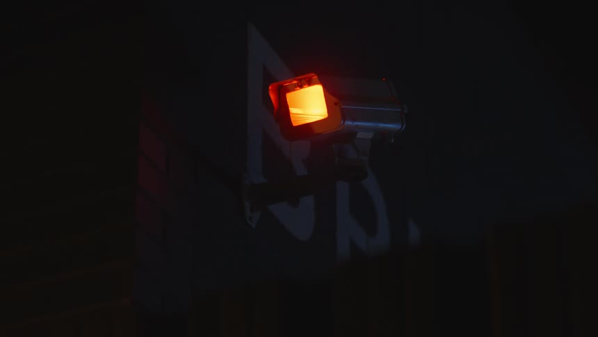 Orange light blinks from a camera attached to the wall at night