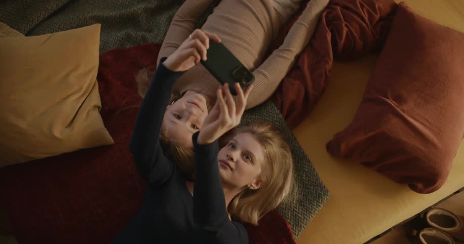 Two young girls lying in bed taking a selfie with an iphone