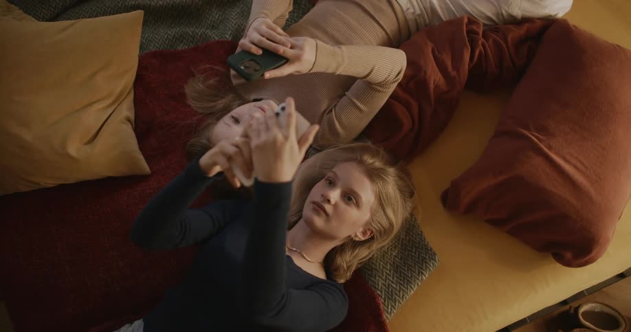 A young adult next to a teenager both lying in bed and using their cell phones